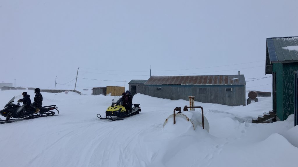 Snowmobiles passing by small buildings